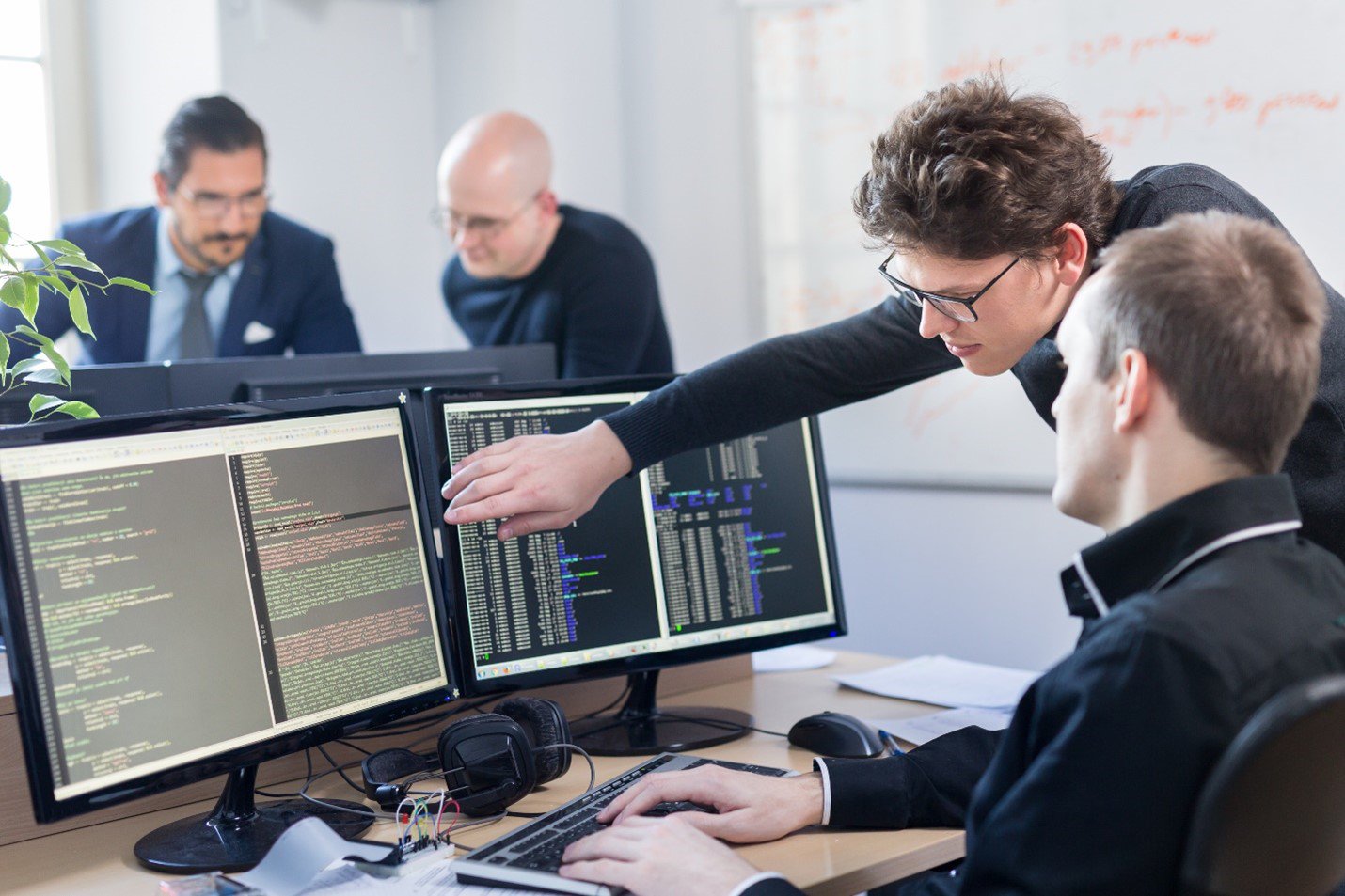 Developers coding on dual monitors, highlighting the need for a dedicated development environment.